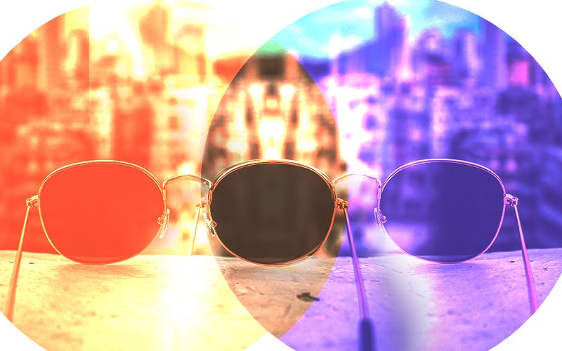 View through three different sunglasses lenses showing varying color tints and clarity levels, illustrating the effect of lens polarization and tint on visual perception of a cityscape.