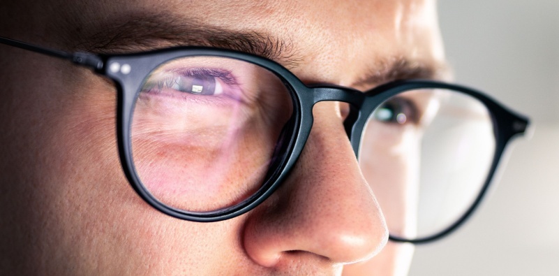 Close-up shot of a person wearing glasses, highlighting the reflection on the lenses and a focused expression
