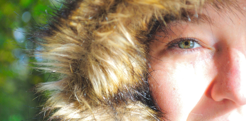 Close up of a woman outside wearing a fur-lined coat hood focusing on her eye.