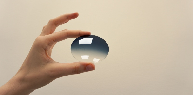 A person holding a gradient tinted eyeglasses lens.