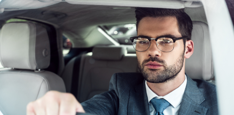 Man in a suit wearing glasses, driving with a focused expression