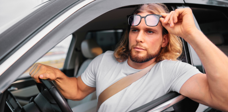 Man lifting glasses above his eyes while sitting in a car, looking out of the window.