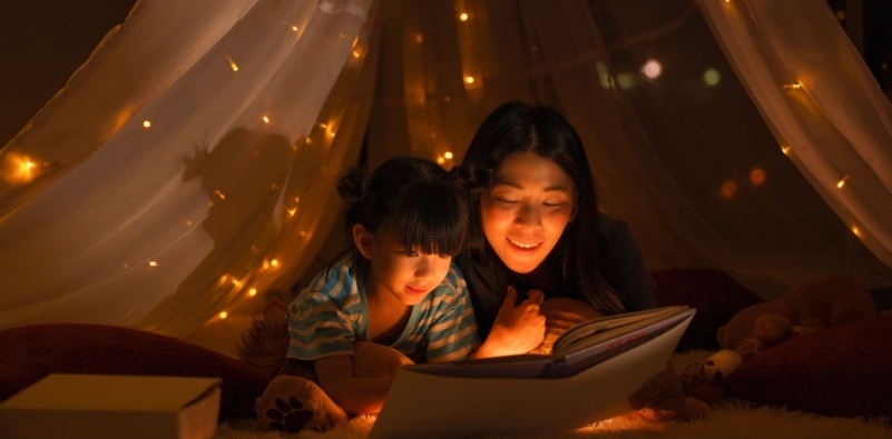 Mother and child reading a book in low lighting.