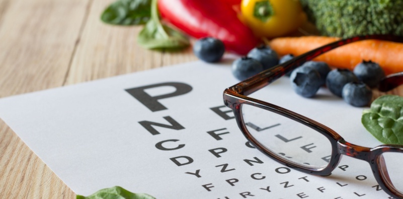 Colorful vegetables and fruits, rich in lutein, eyeglasses and eye test chart on wooden background
