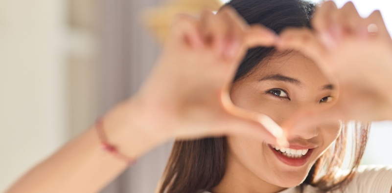 Smiling woman framing face with heart-shaped hands
